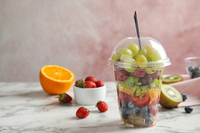 Photo of Fresh tasty fruit salad in plastic cup on white marble table. Space for text