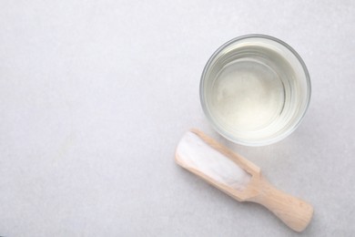 Photo of Vinegar in glass, baking soda and wooden scoop on light table, top view. Space for text