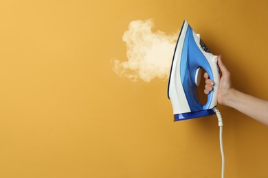 Image of Woman holding modern iron with steam on orange background, closeup. Space for text