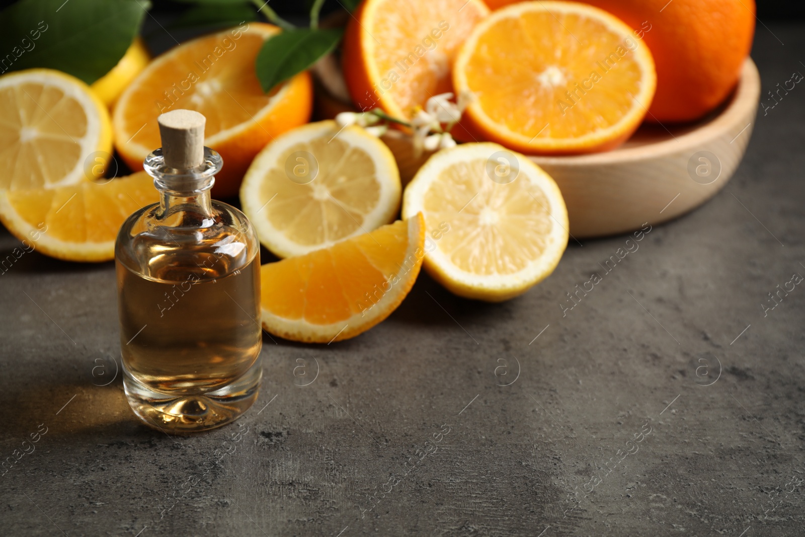 Photo of Bottle of essential oil and citrus fruits on grey table. Space for text