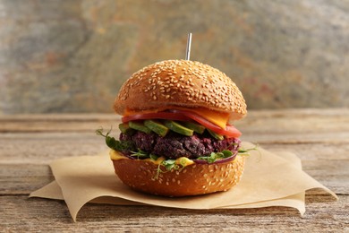 Photo of Tasty vegetarian burger with beet cutlet, cheese, avocado and tomato on wooden table