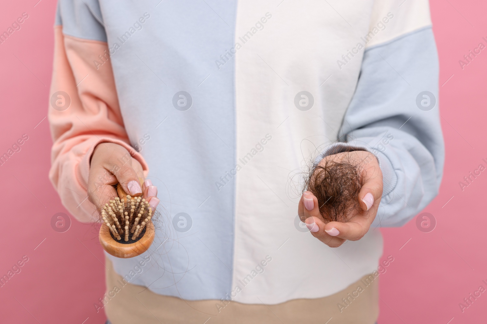 Photo of Woman holding brush with lost hair on pink background, closeup. Alopecia problem