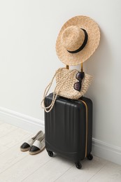 Photo of Suitcase packed for trip, shoes and summer accessories near white wall indoors