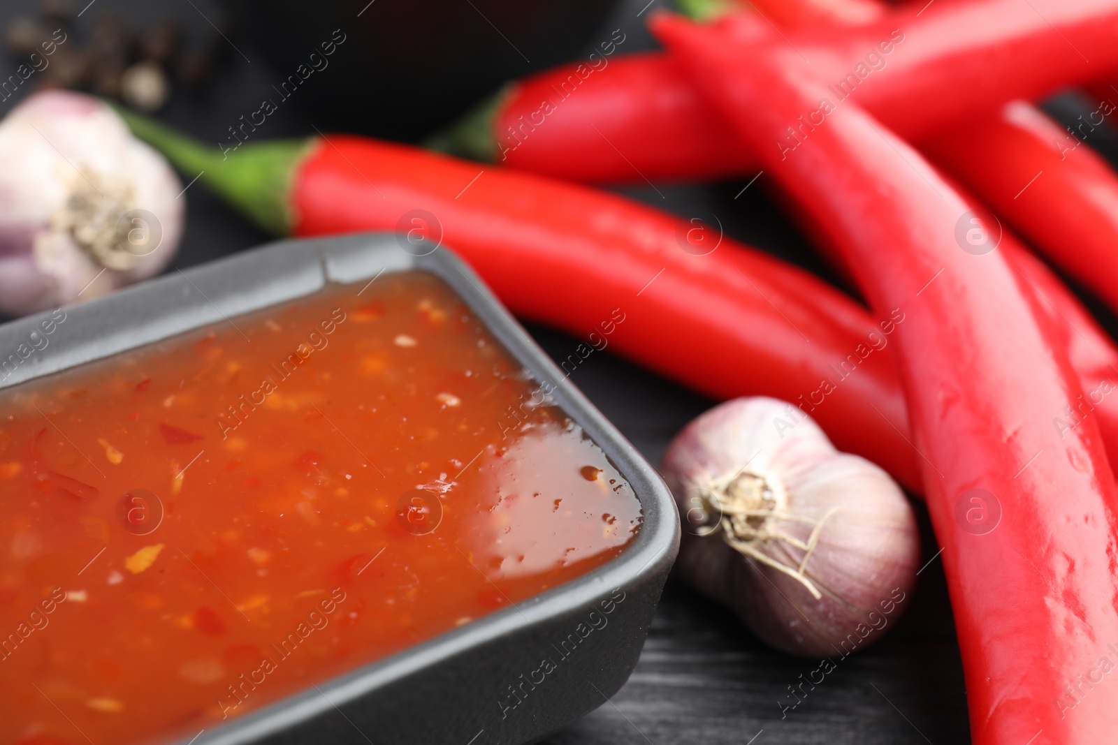 Photo of Spicy chili sauce in bowl, garlic and peppers on table, closeup