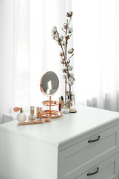 Small mirror and different makeup products on chest of drawers indoors