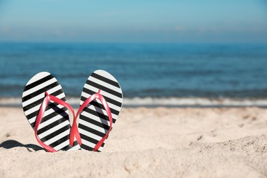 Striped flip flops in sand on beach near sea. Space for text