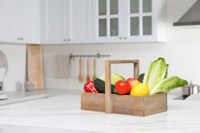 Wooden crate with fresh ripe vegetables and fruits on white table in kitchen, space for text