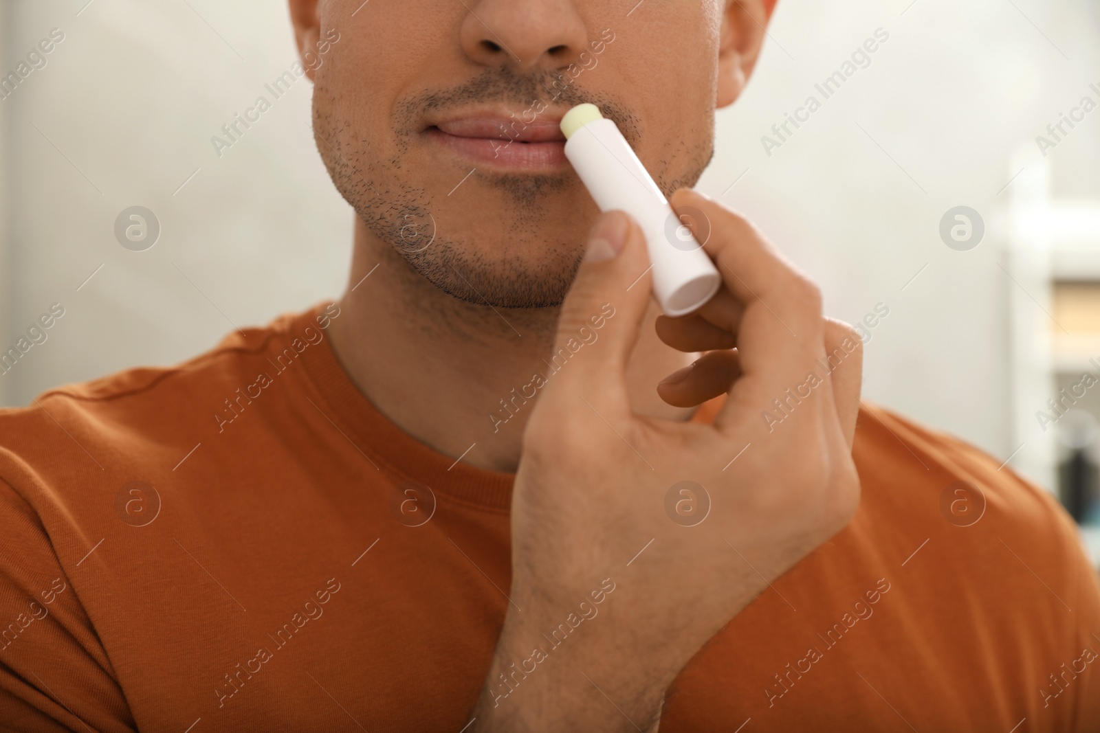 Photo of Man applying hygienic lip balm indoors, closeup