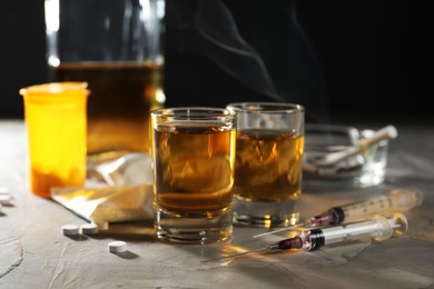 Alcohol and drug addiction. Whiskey in glasses, syringes, pills and cocaine on grey table