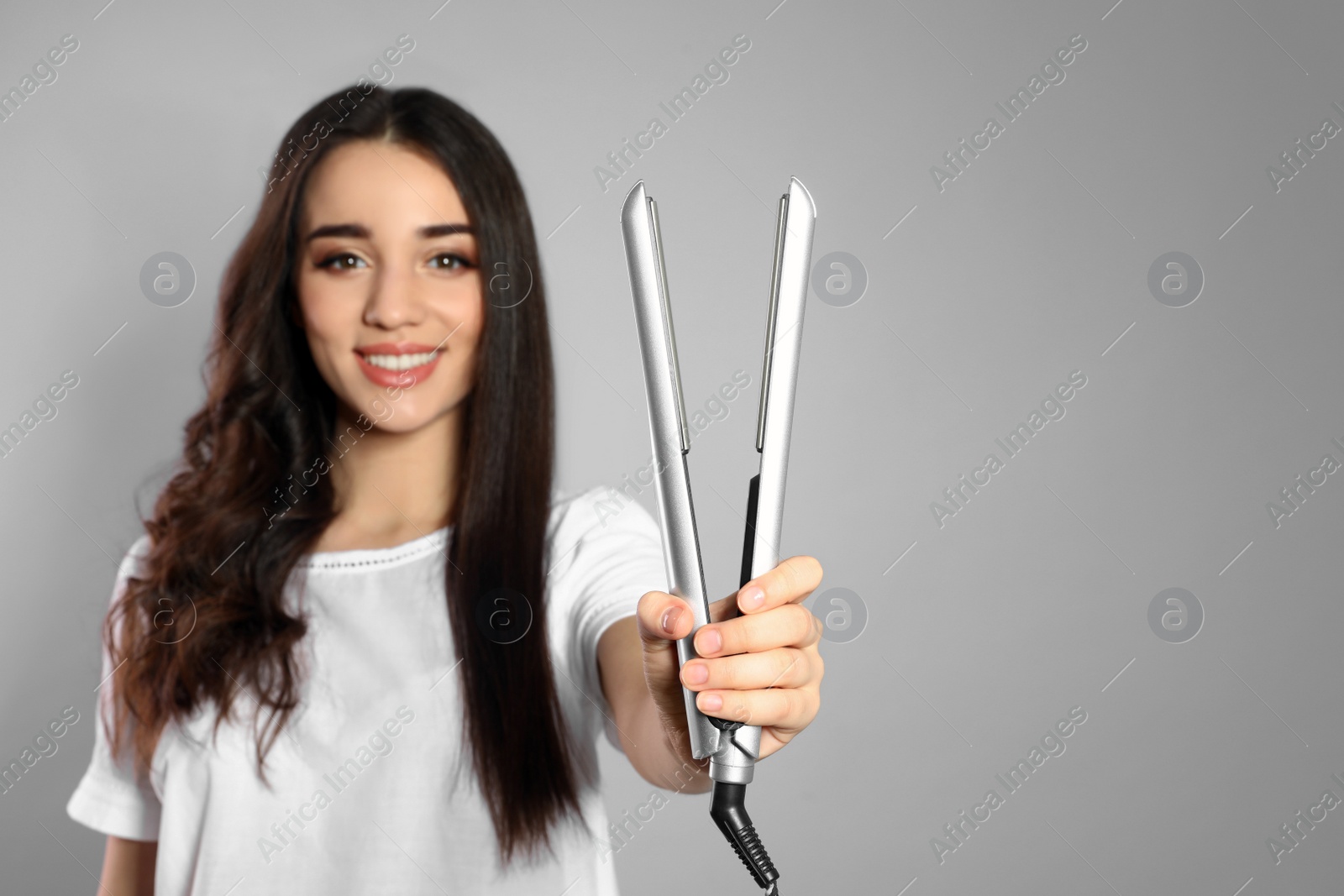 Photo of Happy woman with hair iron on grey background. Space for text