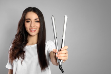 Happy woman with hair iron on grey background. Space for text