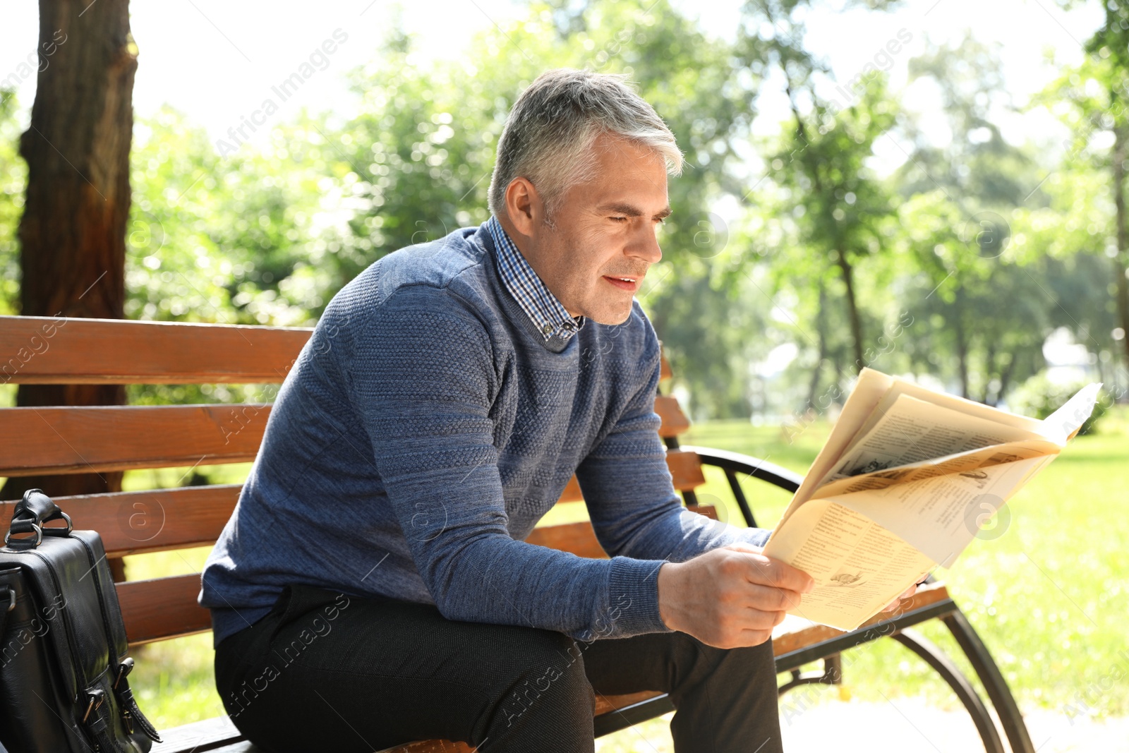 Photo of Portrait of handsome man reading newspaper in park
