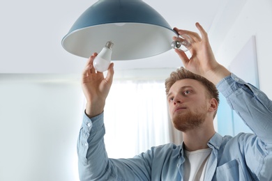 Man changing light bulb in pendant lamp indoors