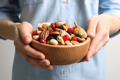 Photo of Young woman holding bowl with different dried fruits and nuts, closeup
