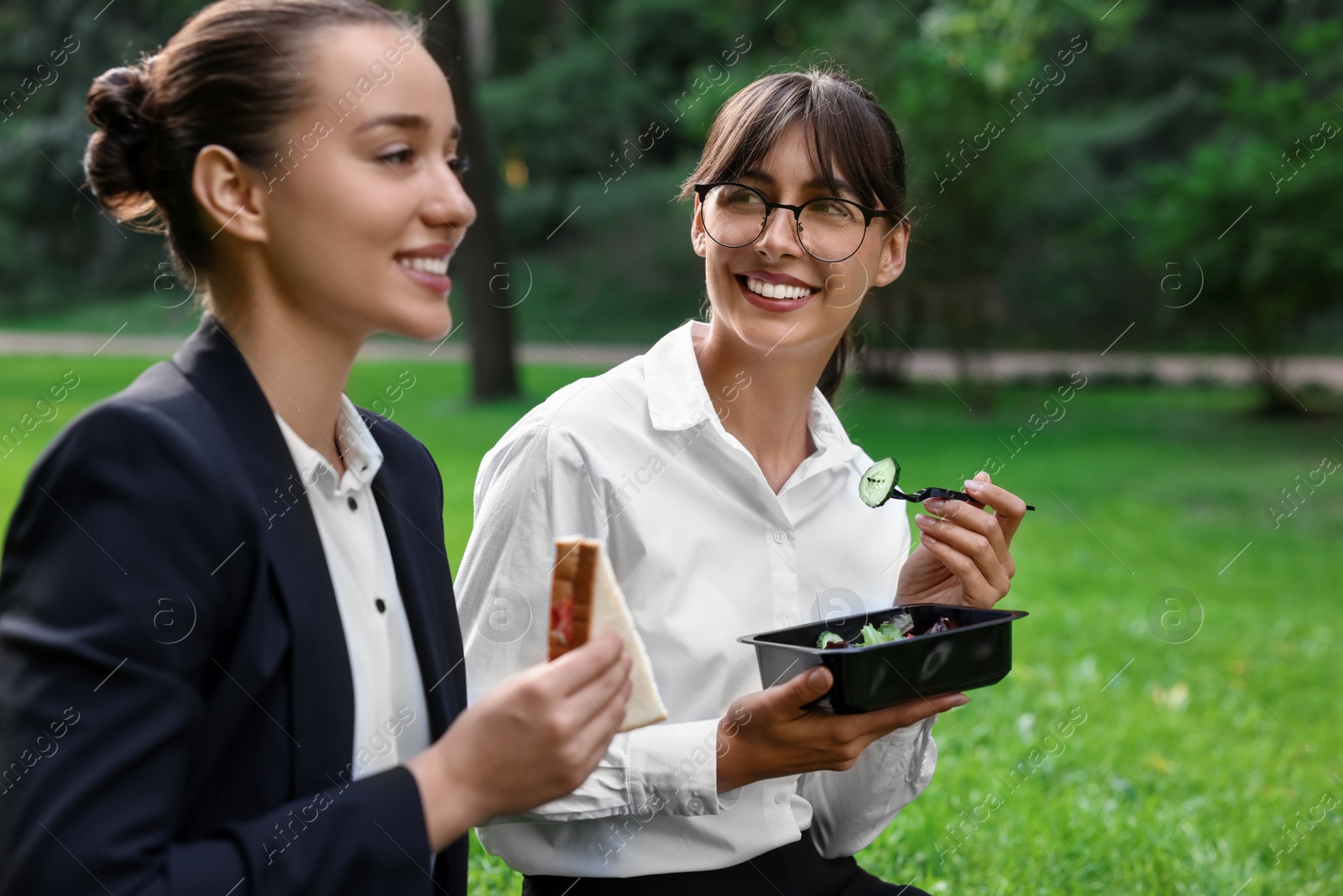 Photo of Happy colleagues having business lunch on green grass in park