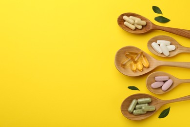 Photo of Different vitamin pills in spoons and green leaves on yellow background, flat lay. Space for text