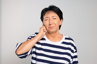 Photo of Senior woman suffering from ear pain on light grey background