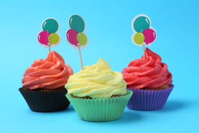 Photo of Delicious cupcakes with bright cream and toppers on light blue background