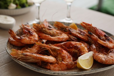 Photo of Plate of delicious cooked shrimps served with lemon and wine at table, closeup