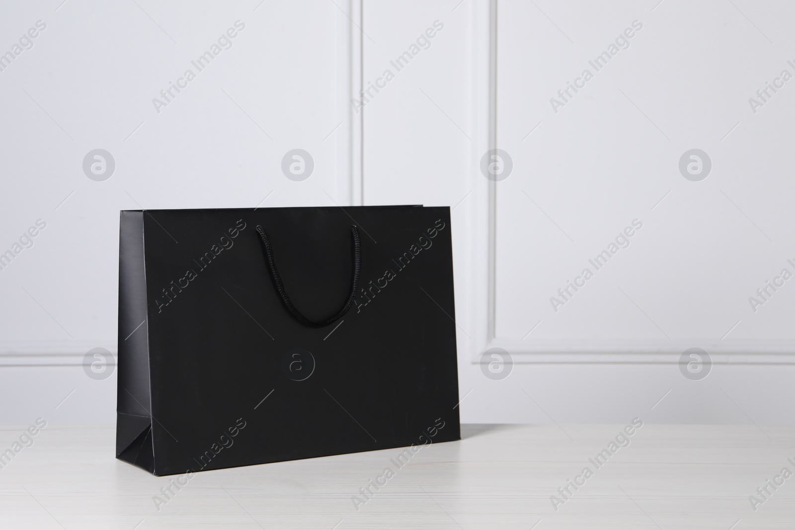 Photo of Black paper bag on white wooden table, space for text