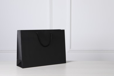 Black paper bag on white wooden table, space for text