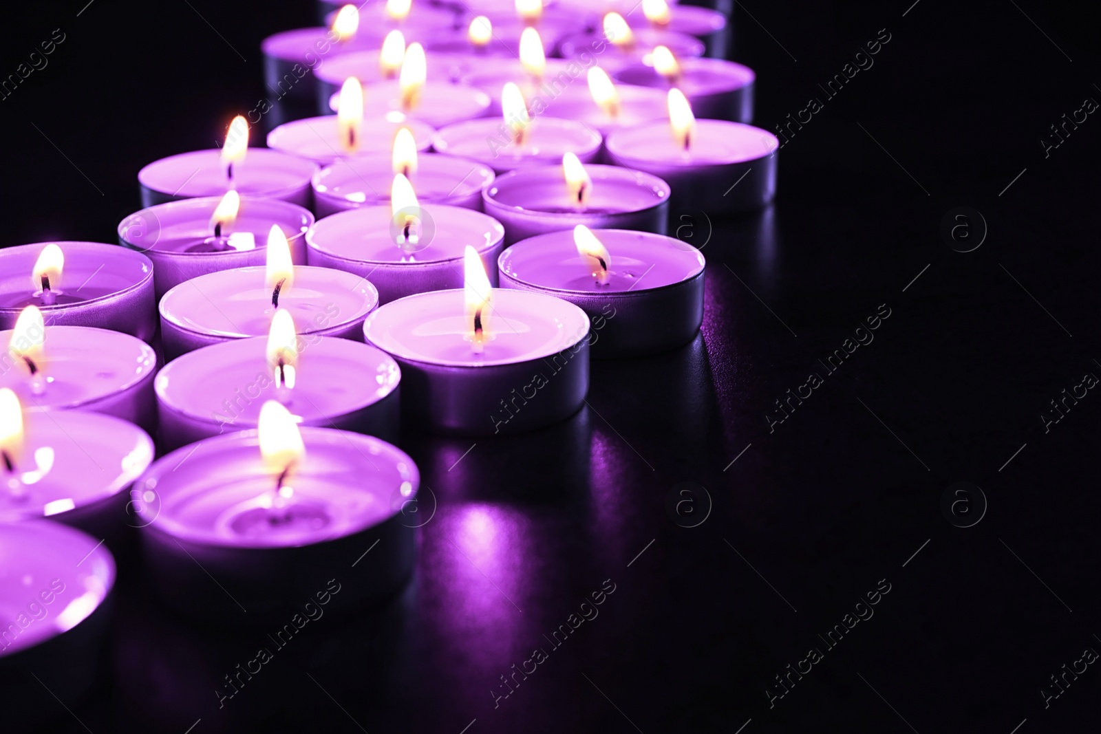 Image of Beautiful burning violet candles on black background. Funeral attributes