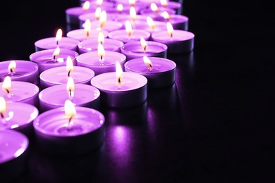 Image of Beautiful burning violet candles on black background. Funeral attributes