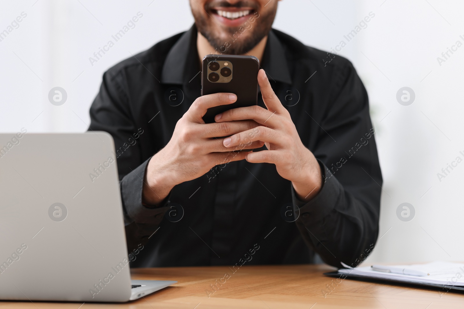 Photo of Man using smartphone at wooden table in office, closeup