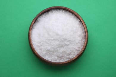 Photo of Bowl of sea salt on green background, top view