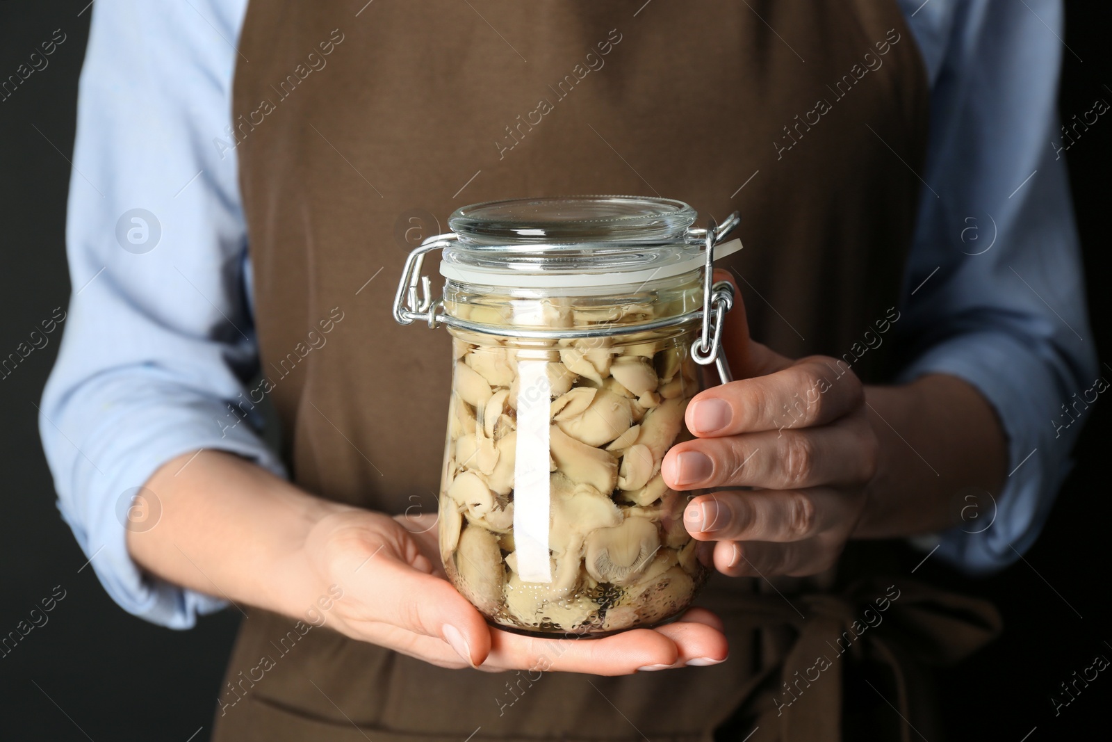 Photo of Woman holding glass jar of pickled mushrooms on black background, closeup