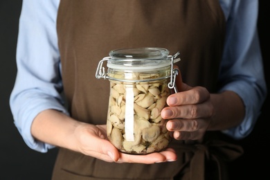 Photo of Woman holding glass jar of pickled mushrooms on black background, closeup