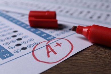 School grade. Answer sheet with red letter A, plus symbol and marker on wooden table, closeup