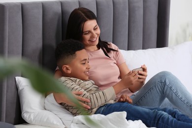 Mother and her African American son using smartphone on bed at home. International family