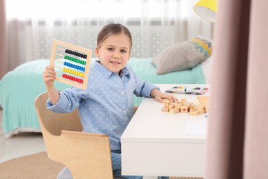 Cute little girl with colorful wooden abacus at desk in room. Home workplace