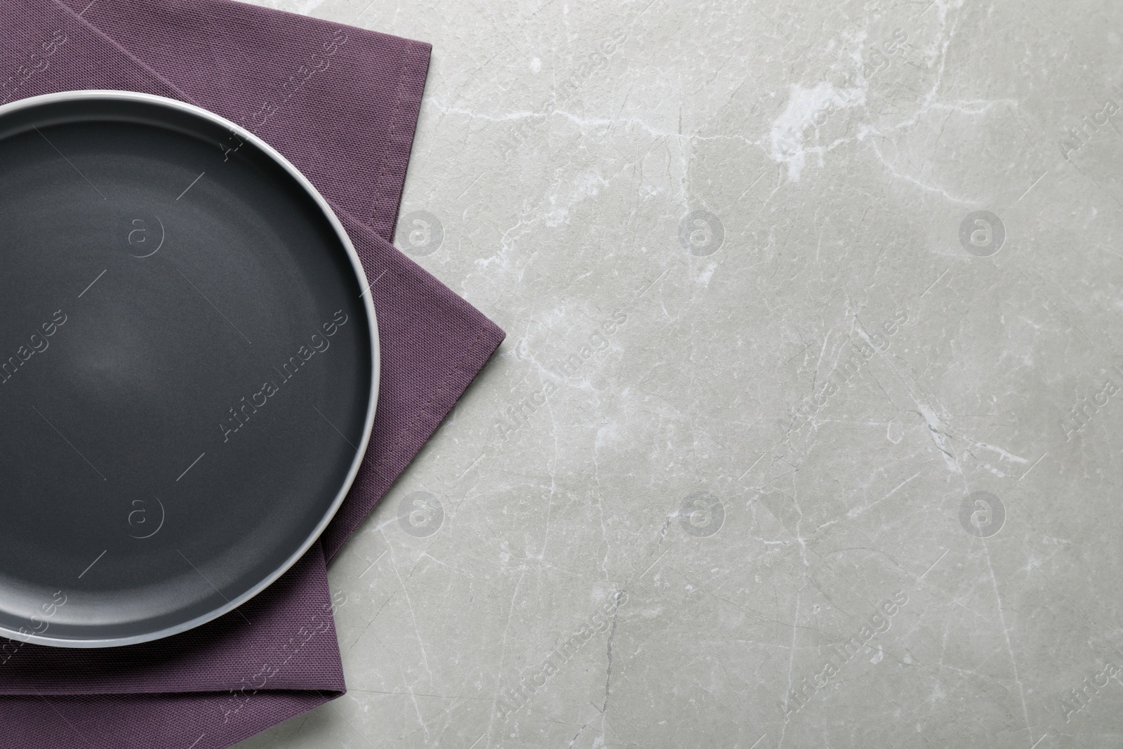 Photo of New dark plate and napkin on light grey table, top view. Space for text