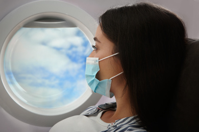 Image of Traveling by airplane during coronavirus pandemic. Woman with face mask near porthole