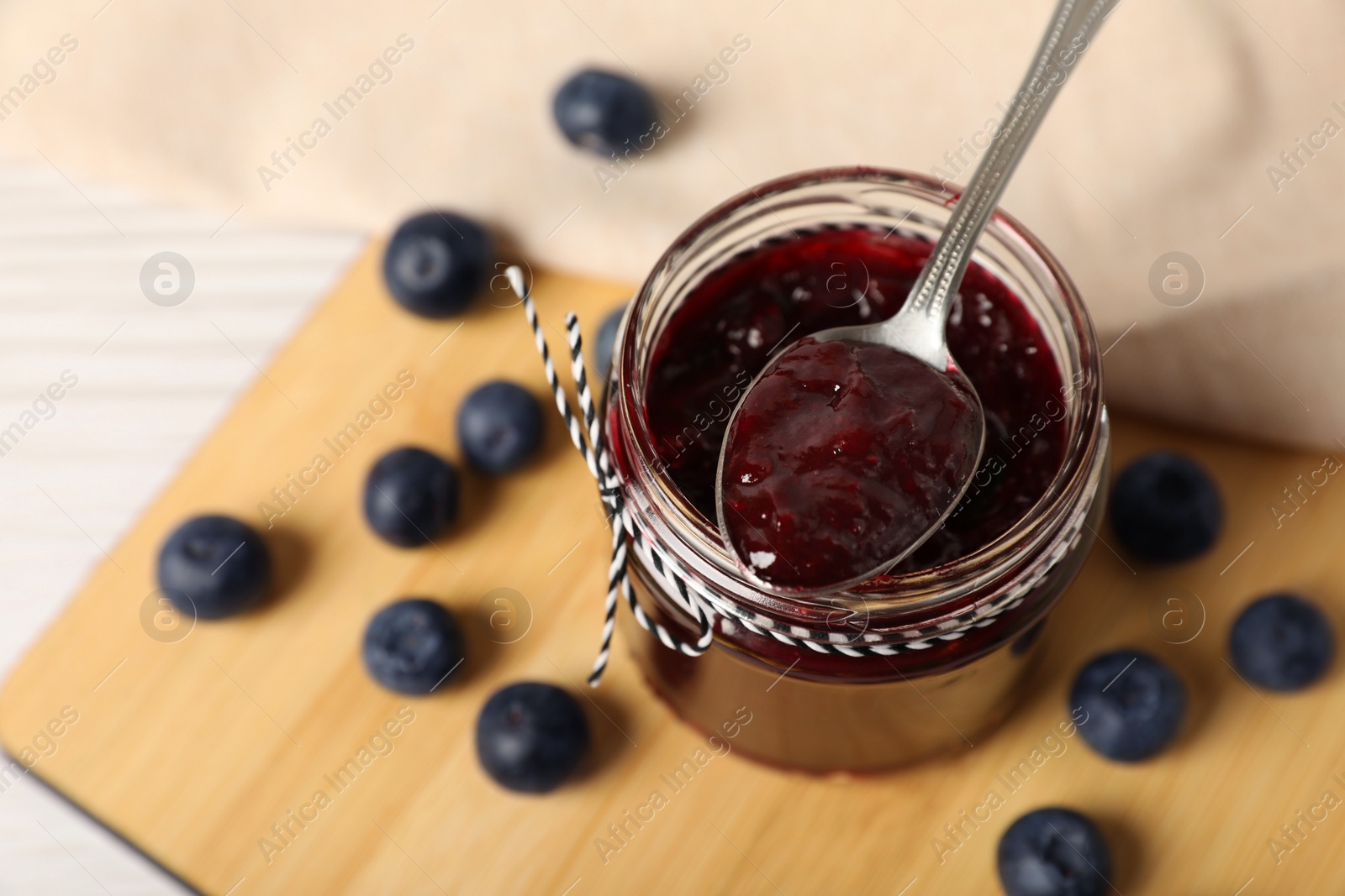 Photo of Spoon with delicious blueberry jam and fresh berries on wooden table, above view. Space for text