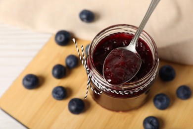 Photo of Spoon with delicious blueberry jam and fresh berries on wooden table, above view. Space for text