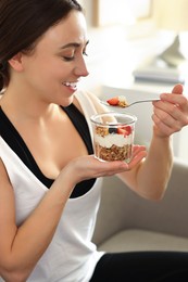 Photo of Woman eating tasty granola with fresh berries and yogurt at home