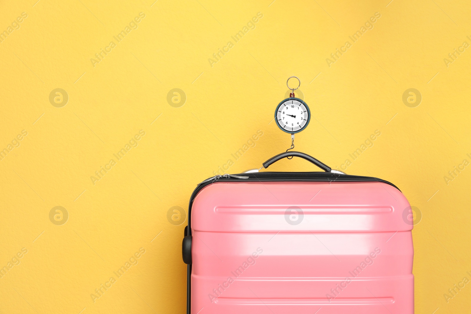 Photo of Modern suitcase and hanging scales against color background, space for text