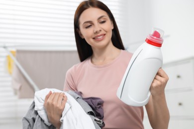 Photo of Woman holding fabric softener and dirty clothes in bathroom, selective focus. Space for text