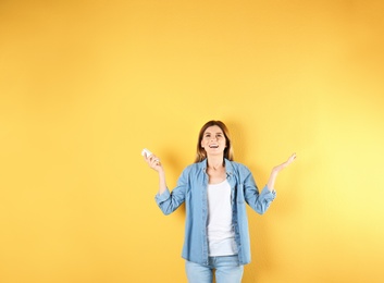 Happy woman with air conditioner remote on color background