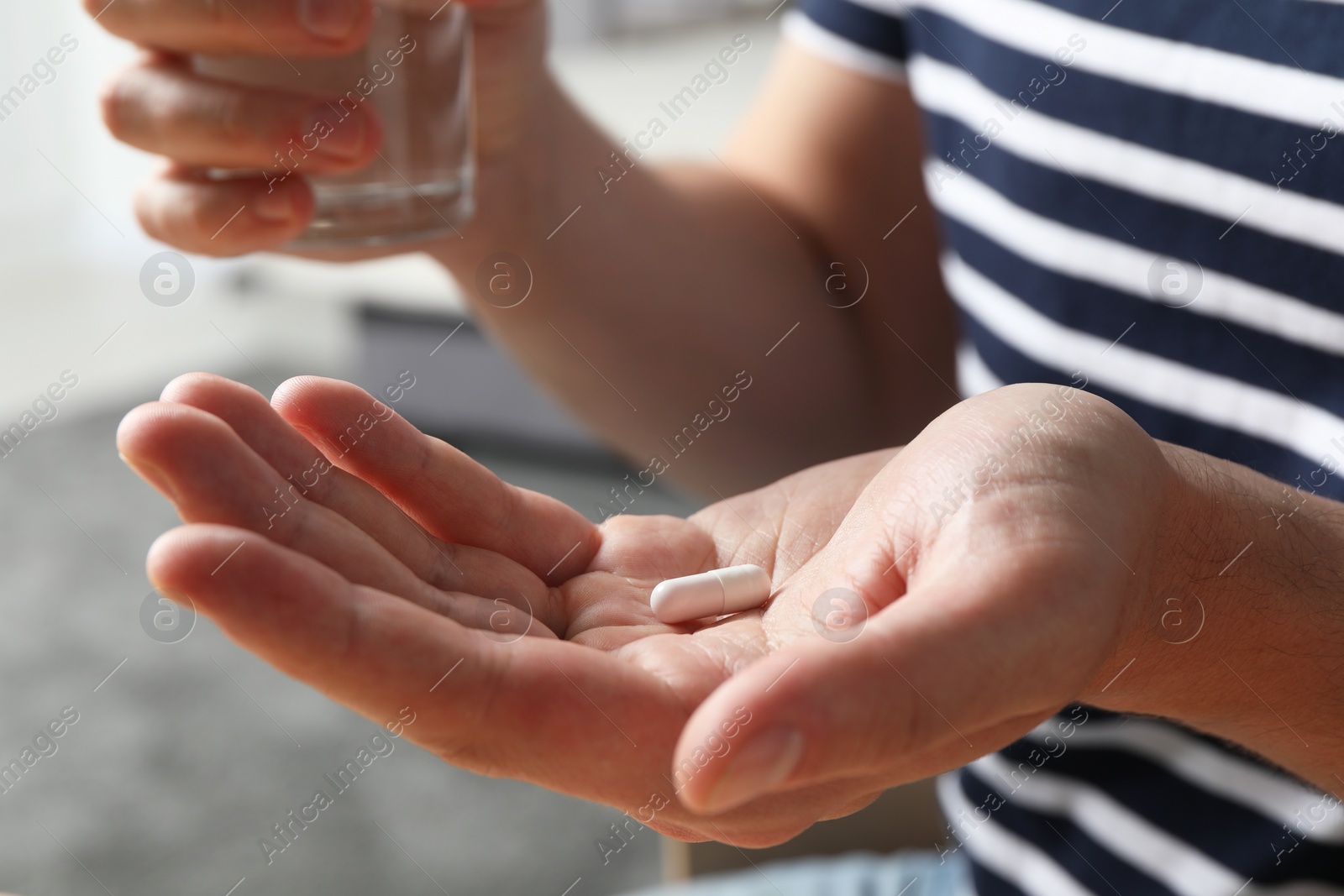 Photo of Man with glass of water and pill on blurred background, closeup