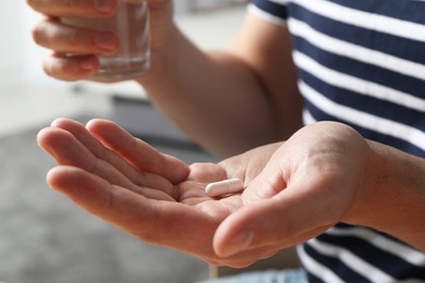 Man with glass of water and pill on blurred background, closeup