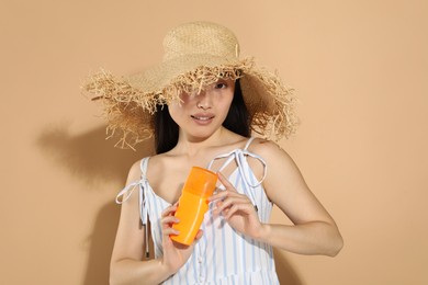 Photo of Beautiful young woman in straw hat holding sun protection cream on beige background