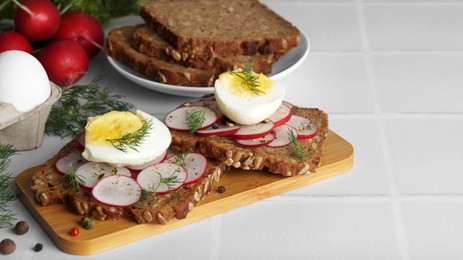 Photo of Tasty sandwiches with boiled egg, radish and ingredients on white tiled table, space for text