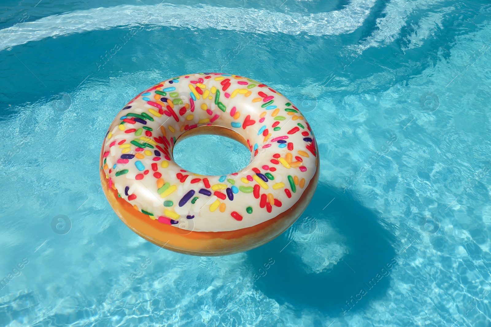 Photo of Bright inflatable doughnut ring floating in swimming pool on sunny day