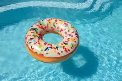 Bright inflatable doughnut ring floating in swimming pool on sunny day