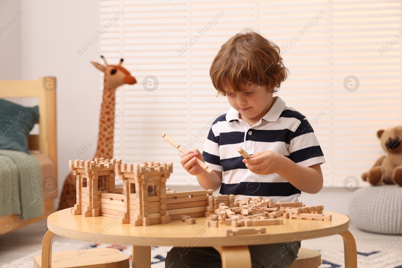 Photo of Cute little boy playing with wooden construction set at table in room. Child's toy