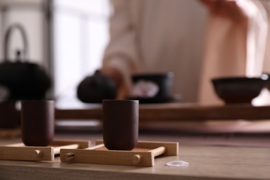 Photo of Master conducting traditional tea ceremony at table indoors, focus on cup